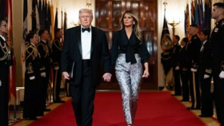 Na foto há Donald Trump do lado de sua esposa. Trump usa um smoking e Melania uma calça prata.