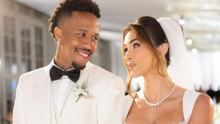 Éder e esposa sorriem um para o outro. Ele usa terno branco. E ela usa vestido de noiva.