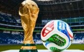 Taça e bola da Copa do Mundo de 2026 em foto, com um estádio no fundo.