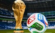 Taça e bola da Copa do Mundo de 2026 em foto, com um estádio no fundo.