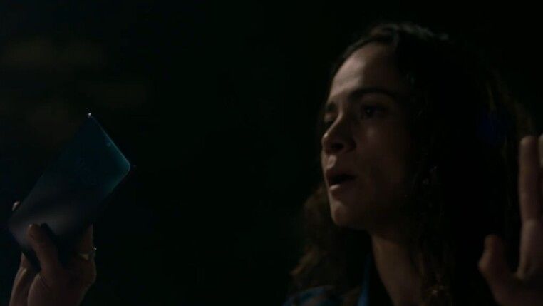 Mulher com a mão para cima enquanto segura celular.