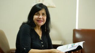Mariangela Hungria segura livro enquanto está sentada olhando para a câmera