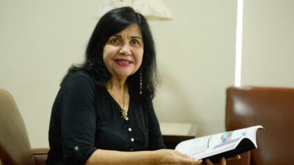 Mariangela Hungria segura livro enquanto está sentada olhando para a câmera