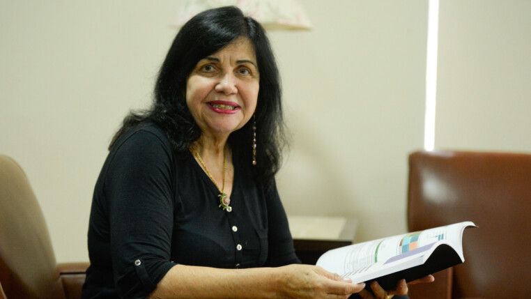 Mariangela Hungria segura livro enquanto está sentada olhando para a câmera