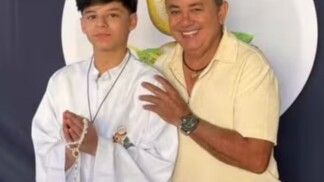 Na foto há um homem e ao seu lado um adolescente com vestimentas comuns da primeira comunhão.