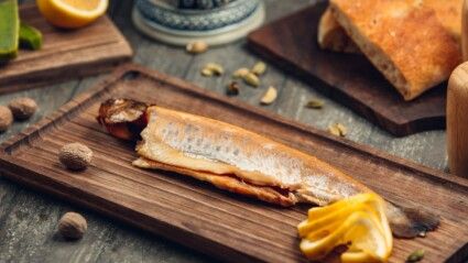 Um peixe cortado em uma mesa com pão e laranja.