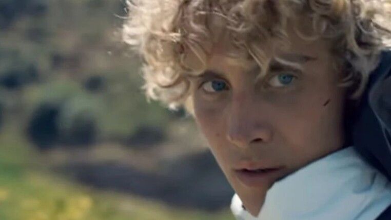 Homem branco com cabelo cacheado loiro olhando para o lado.