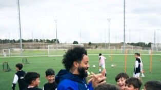 Homem com crianças ao redor dele em um campo de futebol.