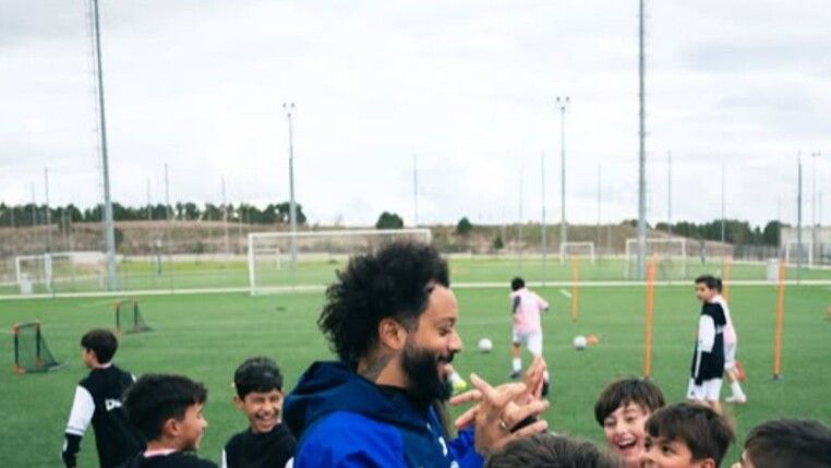 Homem com crianças ao redor dele em um campo de futebol.