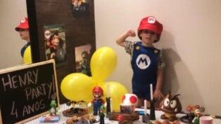 Henry Borel vestido de Mário, ao seu lado têm diversos bonecos e balão amarelo.