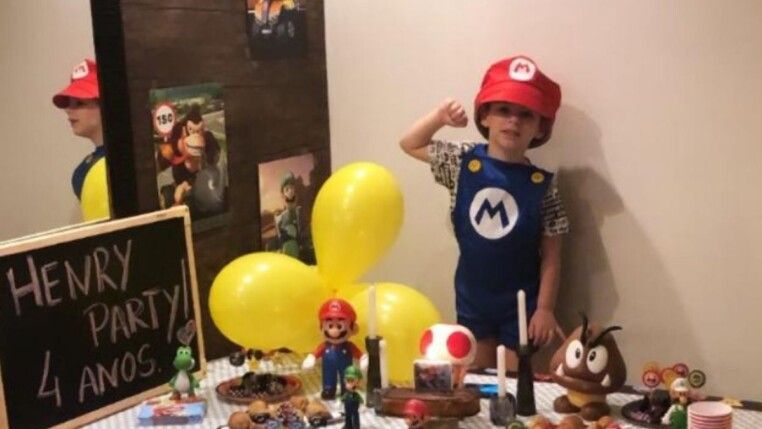 Henry Borel vestido de Mário, ao seu lado têm diversos bonecos e balão amarelo.