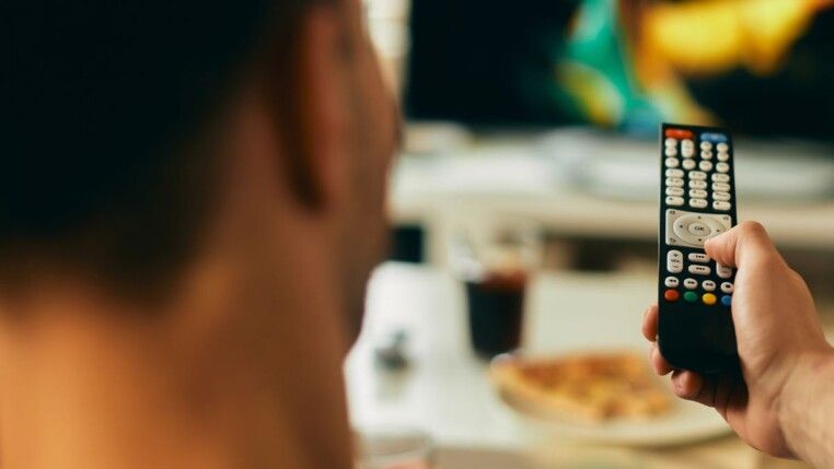 Homem sentado em um sofá com um controle na mão.