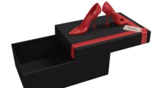 Uma caixa preta com detalhes em vermelho e na tampa há um par de salto vermelho.