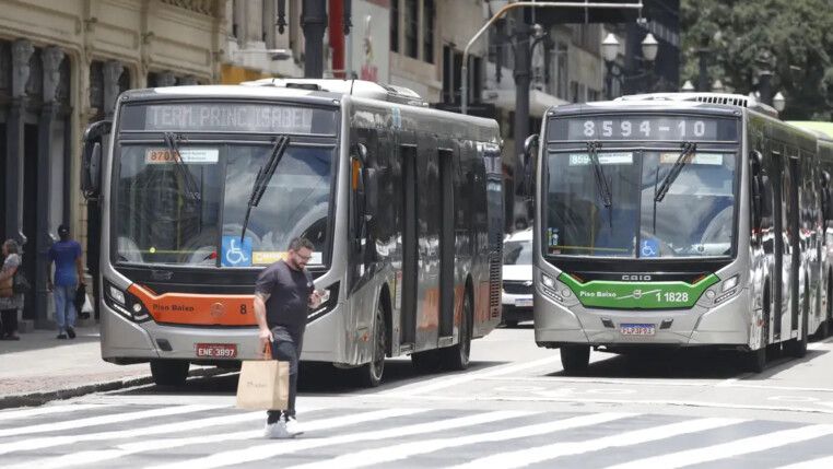 Dois ônibus param diante de um pedestre na faixa