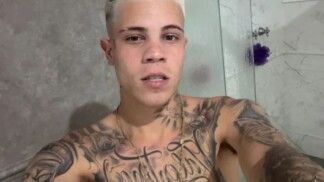 Homem de cabelo platinado e sem camiseta com diversas tatuagens.