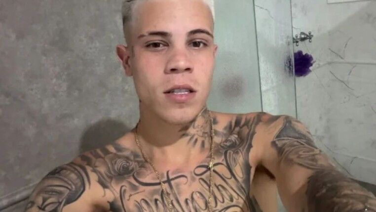 Homem de cabelo platinado e sem camiseta com diversas tatuagens.