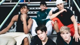 Na foto há 4 homens, eles usam regata e bermuda, outros usam camiseta preta.