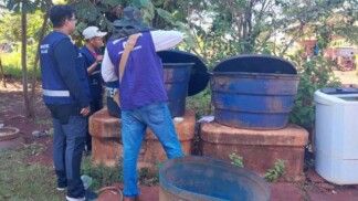 Três agentes de saúde realizando uma inspeção de vigilância sanitária em uma área externa, possivelmente no quintal de uma residência.