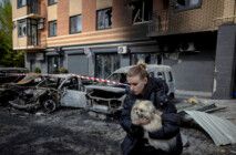 Drones Mulher carrega cachorro à frente de um prédio atingido por drones