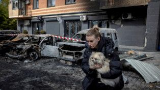 Mulher carrega cachorro à frente de um prédio atingido por drones