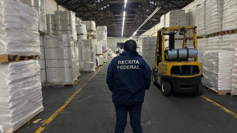 Agente da Receita Federal está de costas para a câmera e de frente para diversos blocos de plástico