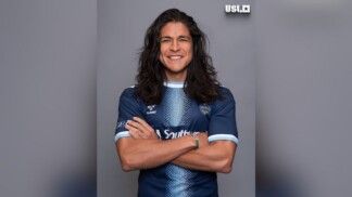 Ator cruza os braços e está vestido com camisa do clube de futebol
