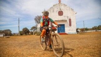 Eliana Tamietti de bicicleta, posando para foto em frente a uma capela