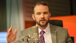 Dario Durigan gesticula enquanto fala ao microfone durante entrevista