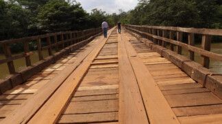 Duas pessoas caminham sobre uma ponte de madeira