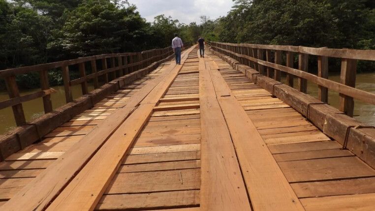 Duas pessoas caminham sobre uma ponte de madeira