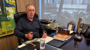 Ancelotti está sentado à frente de sua mesa de trabalho, gesticulando com as duas mãos