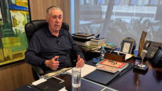 Ancelotti está sentado à frente de sua mesa de trabalho, gesticulando com as duas mãos