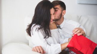 Menino que beija sua namorada na bochecha, enquanto ela abre um saco vermelho