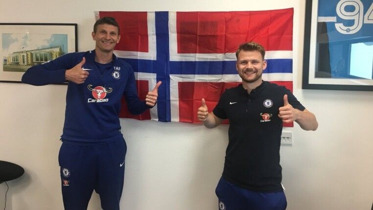 Tore André Flo (à esq.) ao lado de membro do staff do Chelsea e uma bandeira da Noruega na parede