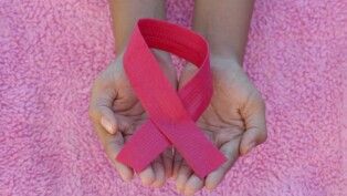 Mãos segurando um laço rosa, o símbolo universal da conscientização e prevenção do câncer de mama