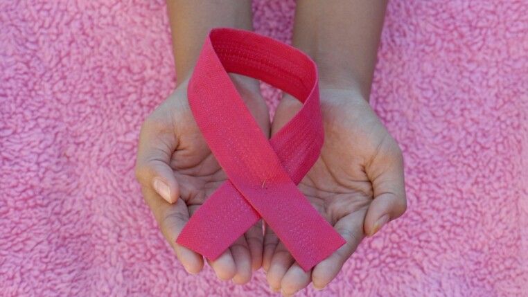 Mãos segurando um laço rosa, o símbolo universal da conscientização e prevenção do câncer de mama