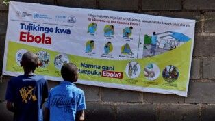 As crianças congolesas Ibrah Asimwe e Alex Uketi leem um cartaz informativo enquanto agências humanitárias intensificam os esforços para conter um novo surto de ebola causado pela variante Bundibugyo, em Bunia, na província de Ituri, na República Democrática do Congo