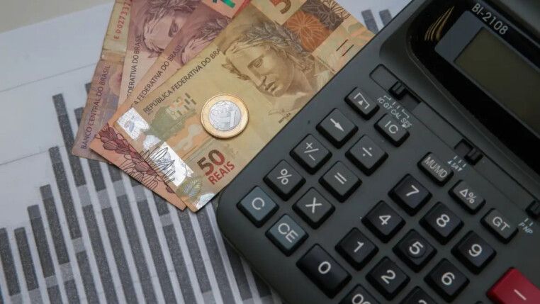 Notas de 50 reais, moedas, e um teclado na imagem