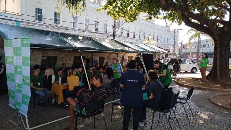 Diversas pessoas sentadas debaixo de tenda sendo atendidas