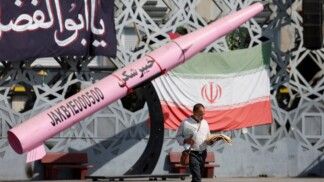 Um homem caminha ao lado de uma réplica simbólica de um míssil iraniano e de uma bandeira do Irã na Praça Imam Hussein, em Teerã, Irã, em 12/07/2026