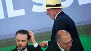 O presidente Luiz Inácio Lula da Silva reage durante cerimônia de sanção do projeto de lei que cria uma linha de crédito para empresas afetadas pelas novas tarifas impostas pelo governo dos Estados Unidos. À frente, aparecem o vice-presidente Geraldo Alckmin e o ministro da Fazenda, Dario Durigan. A cerimônia foi realizada no Palácio do Planalto, em Brasília, em 22/07/2026.