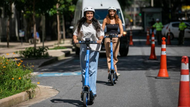 Duas garotas passeando em um patinete. A novidade agora vai chegar na Pampulha, um dos principais pontos turísticos da capital mineira.