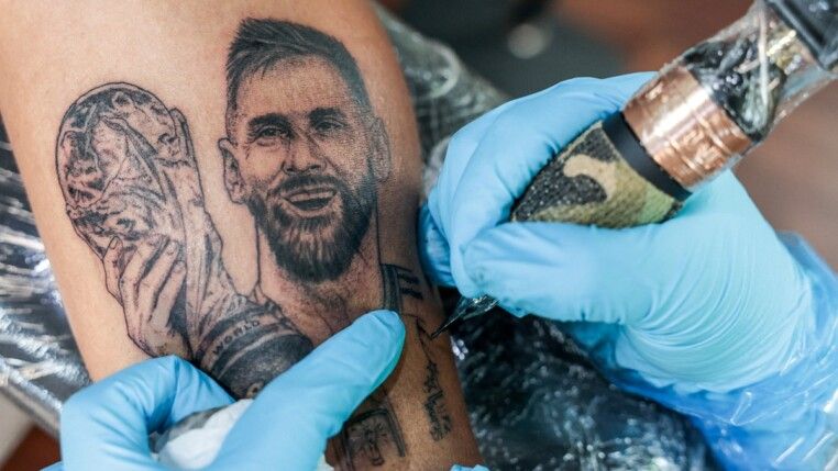 A tatuadora Patcharakul Jungsakul, de 42 anos, fã do jogador argentino Lionel Messi, faz uma tatuagem do atacante no braço esquerdo de Athirat Koenmuang, de 35 anos. Ela oferece tatuagens de Messi por um valor simbólico a outros fãs do craque antes da final da Copa do Mundo da FIFA 2026 entre Espanha e Argentina, em seu estúdio de tatuagem, em Bangkok, Tailândia, em 17/07/2026.